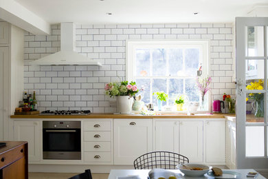 Large rural grey and cream single-wall kitchen/diner in Sussex with shaker cabinets, white cabinets, wood worktops, white splashback, metro tiled splashback, stainless steel appliances, light hardwood flooring, a built-in sink and no island.