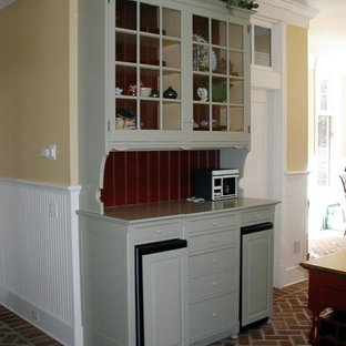 This is an example of a large traditional galley eat-in kitchen in Other with a farmhouse sink, raised-panel cabinets, grey cabinets, soapstone benchtops, black splashback, stone slab splashback, stainless steel appliances, brick floors, with island and red floor.