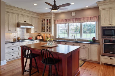 Example of a mid-sized country l-shaped medium tone wood floor and beige floor eat-in kitchen design in Philadelphia with an undermount sink, shaker cabinets, light wood cabinets, wood countertops, beige backsplash, porcelain backsplash, stainless steel appliances and an island