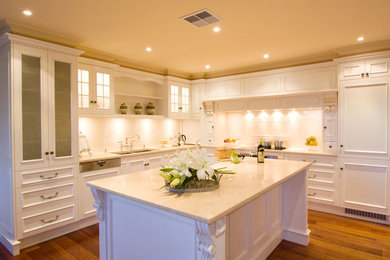Пример оригинального дизайна: угловая кухня в классическом стиле с двойной мойкой, белыми фасадами, белым фартуком, фартуком из плитки кабанчик, техникой под мебельный фасад, паркетным полом среднего тона и островом