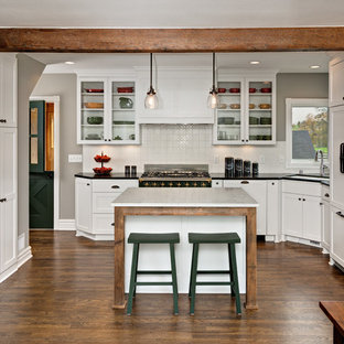 Foto de cocina en L, de estilo de casa de campo, de tamaño medio, abierta, con fregadero bajoencimera, armarios estilo shaker, puertas de armario blancas, salpicadero blanco, suelo de madera oscura, una isla, encimera de esteatita, salpicadero de azulejos de cerámica y electrodomésticos con paneles