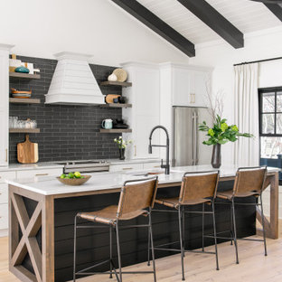 Photo of a farmhouse galley kitchen in Charleston with a submerged sink, shaker cabinets, white cabinets, engineered stone countertops, black splashback, porcelain splashback, stainless steel appliances, light hardwood flooring, an island, white worktops and exposed beams.