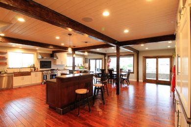 Large rural u-shaped kitchen/diner in Seattle with a belfast sink, shaker cabinets, white cabinets, composite countertops, white splashback, metro tiled splashback, stainless steel appliances, medium hardwood flooring and an island.