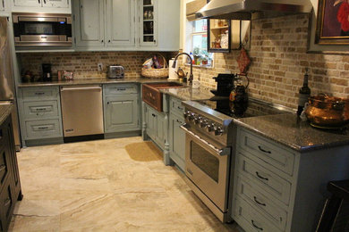 Lantlig inredning av ett kök, med en rustik diskho, luckor med upphöjd panel, gröna skåp, granitbänkskiva, stänkskydd i tegel, rostfria vitvaror, en köksö och beiget golv