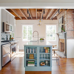 Modelo de cocina de galera, de estilo de casa de campo, pequeña, con fregadero sobremueble, armarios estilo shaker, puertas de armario grises, encimera de cuarzo compacto, salpicadero azul, salpicadero de azulejos de terracota, electrodomésticos de acero inoxidable, suelo de madera en tonos medios, una isla y suelo marrón