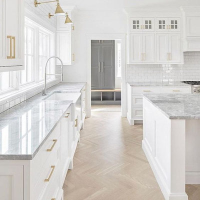 Inspiration for a large cottage l-shaped light wood floor and brown floor open concept kitchen remodel in Columbus with a farmhouse sink, white cabinets, marble countertops, white backsplash, subway tile backsplash, stainless steel appliances, white countertops, an island and shaker cabinets