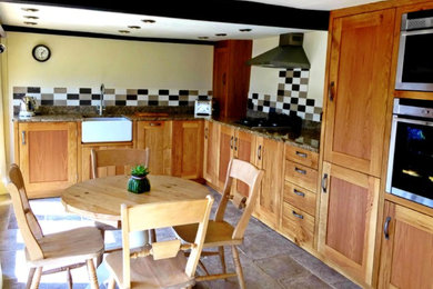 This is an example of a medium sized rural l-shaped kitchen/diner in Devon with a submerged sink, shaker cabinets, medium wood cabinets, granite worktops, multi-coloured splashback, ceramic splashback, stainless steel appliances and slate flooring.