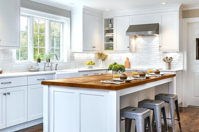 Example of a mid-sized transitional l-shaped medium tone wood floor and brown floor enclosed kitchen design in Other with a farmhouse sink, white cabinets, quartz countertops, white backsplash, ceramic backsplash, an island, shaker cabinets and stainless steel appliances
