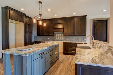 Example of a large cottage l-shaped porcelain tile eat-in kitchen design in Austin with a farmhouse sink, recessed-panel cabinets, dark wood cabinets, granite countertops, gray backsplash, ceramic backsplash, stainless steel appliances and an island