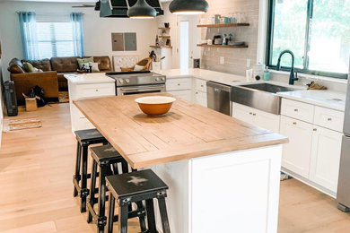 Inspiration for a large farmhouse l-shaped laminate floor and beige floor eat-in kitchen remodel in Austin with a farmhouse sink, shaker cabinets, white cabinets, quartzite countertops, gray backsplash, glass tile backsplash, stainless steel appliances, an island and white countertops