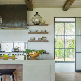 Mid-sized country l-shaped eat-in kitchen in Burlington with an undermount sink, flat-panel cabinets, beige cabinets, concrete benchtops, white splashback, porcelain splashback, stainless steel appliances, light hardwood floors, with island and beige benchtop.