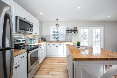 Inspiration for a mid-sized country l-shaped medium tone wood floor and beige floor eat-in kitchen remodel in New York with an undermount sink, shaker cabinets, white cabinets, wood countertops, white backsplash, subway tile backsplash, stainless steel appliances, an island and brown countertops