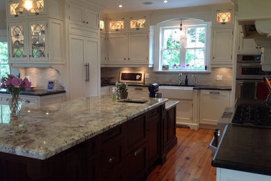 Eat-in kitchen - traditional u-shaped medium tone wood floor eat-in kitchen idea in Toronto with a farmhouse sink, beaded inset cabinets, white cabinets, granite countertops, beige backsplash, stone tile backsplash, stainless steel appliances and an island