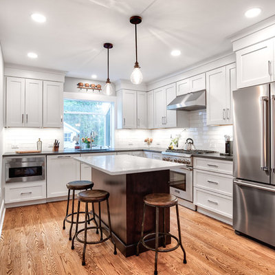 Inspiration for a mid-sized country l-shaped brown floor and medium tone wood floor kitchen remodel in New York with white cabinets, white backsplash, subway tile backsplash, stainless steel appliances, an island, black countertops, an undermount sink, shaker cabinets and soapstone countertops