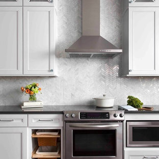 Idee per una grande cucina classica con ante bianche, paraspruzzi con piastrelle in pietra, elettrodomestici in acciaio inossidabile, parquet scuro, ante in stile shaker, top in superficie solida, paraspruzzi bianco, pavimento marrone, top nero e isola
