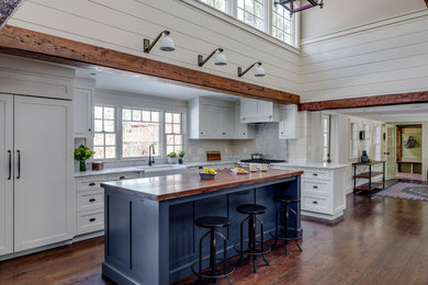 Large farmhouse l-shaped brown floor and medium tone wood floor open concept kitchen photo in Boston with a farmhouse sink, marble countertops, an island, shaker cabinets, blue cabinets, paneled appliances, white countertops, gray backsplash and marble backsplash