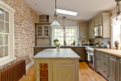 Enclosed kitchen - mid-sized traditional l-shaped medium tone wood floor and brown floor enclosed kitchen idea in Philadelphia with a farmhouse sink, raised-panel cabinets, green cabinets, gray backsplash, stainless steel appliances and an island