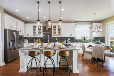Inspiration for a cottage medium tone wood floor and brown floor eat-in kitchen remodel in Tampa with a drop-in sink, recessed-panel cabinets, white cabinets, quartzite countertops, gray backsplash, glass tile backsplash, stainless steel appliances, an island and gray countertops