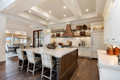 Example of a country dark wood floor and brown floor enclosed kitchen design in Atlanta with a farmhouse sink, recessed-panel cabinets, white cabinets, white backsplash, stone tile backsplash, paneled appliances, an island and white countertops