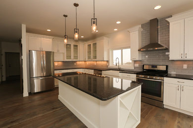 Open concept kitchen - mid-sized traditional l-shaped light wood floor open concept kitchen idea in Other with a farmhouse sink, shaker cabinets, white cabinets, granite countertops, gray backsplash, subway tile backsplash, stainless steel appliances and an island