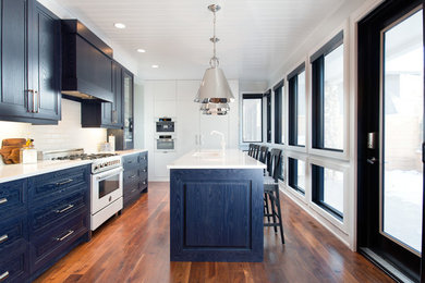 Example of a mid-sized transitional single-wall dark wood floor and brown floor eat-in kitchen design in Other with an undermount sink, raised-panel cabinets, blue cabinets, quartz countertops, white backsplash, subway tile backsplash, white appliances and an island