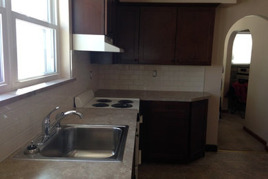 Example of a mid-sized l-shaped linoleum floor eat-in kitchen design in Wilmington with a single-bowl sink, recessed-panel cabinets, dark wood cabinets, laminate countertops, white backsplash, subway tile backsplash, white appliances and no island