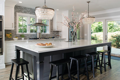 Large elegant galley porcelain tile eat-in kitchen photo in New York with a farmhouse sink, beaded inset cabinets, white cabinets, quartz countertops, gray backsplash, glass tile backsplash, stainless steel appliances and an island