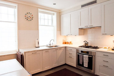 ニューヨークにあるラグジュアリーな中くらいなコンテンポラリースタイルのおしゃれなキッチン (アンダーカウンターシンク、シェーカースタイル扉のキャビネット、白いキャビネット、大理石カウンター、白いキッチンパネル、セラミックタイルのキッチンパネル、パネルと同色の調理設備、濃色無垢フローリング、アイランドなし) の写真