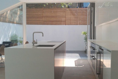 Large contemporary kitchen in London with a submerged sink, white cabinets, engineered stone countertops, stainless steel appliances, light hardwood flooring and an island.