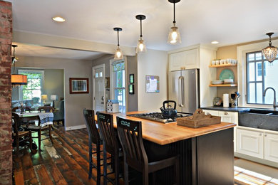 Cette image montre une cuisine parallèle traditionnelle de taille moyenne avec un évier de ferme, des portes de placard blanches, un plan de travail en bois, un sol en bois brun et îlot.