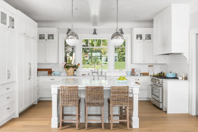 Kitchen - transitional u-shaped medium tone wood floor and brown floor kitchen idea in Vancouver with a farmhouse sink, recessed-panel cabinets, white cabinets, white backsplash, subway tile backsplash, stainless steel appliances, an island and white countertops