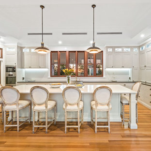 Traditional kitchen in Other with shaker cabinets, beige cabinets, white splashback, stainless steel appliances, light hardwood floors, with island, beige floor and black benchtop.