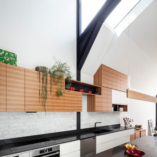 This is an example of a mid-sized contemporary galley eat-in kitchen in Sydney with a double-bowl sink, flat-panel cabinets, white cabinets, quartz benchtops, grey splashback, stainless steel appliances, concrete floors, with island, grey floor and black benchtop.