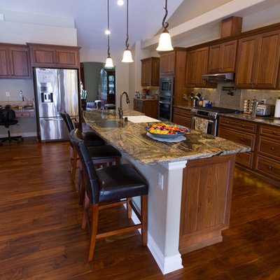 Open concept kitchen - large craftsman galley medium tone wood floor and brown floor open concept kitchen idea in Seattle with a farmhouse sink, raised-panel cabinets, medium tone wood cabinets, granite countertops, beige backsplash, ceramic backsplash, stainless steel appliances and an island