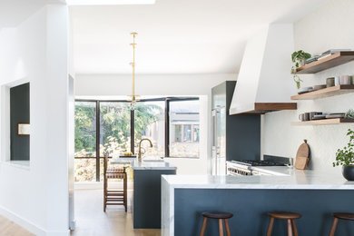 Example of a mid-sized danish l-shaped light wood floor and brown floor enclosed kitchen design in San Francisco with a farmhouse sink, flat-panel cabinets, blue cabinets, granite countertops, white backsplash, porcelain backsplash, stainless steel appliances, an island and gray countertops