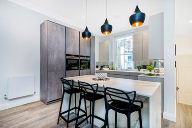 Inspiration for a small contemporary l-shaped open plan kitchen in London with a built-in sink, flat-panel cabinets, grey cabinets, grey splashback, mirror splashback, integrated appliances, laminate floors, an island and brown floors.