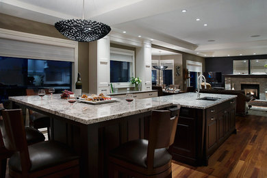 Example of a large classic u-shaped medium tone wood floor eat-in kitchen design in Calgary with a drop-in sink, beaded inset cabinets, dark wood cabinets, granite countertops, stainless steel appliances, two islands and white backsplash