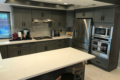 Example of a minimalist u-shaped eat-in kitchen design with recessed-panel cabinets, gray cabinets, quartzite countertops, gray backsplash, marble backsplash, stainless steel appliances, a peninsula and white countertops