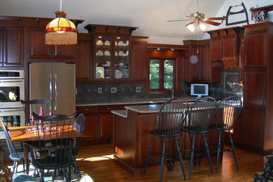 Inspiration for a large timeless l-shaped medium tone wood floor and brown floor eat-in kitchen remodel in New York with an undermount sink, raised-panel cabinets, granite countertops, stainless steel appliances, an island, dark wood cabinets, multicolored backsplash, stone tile backsplash and gray countertops