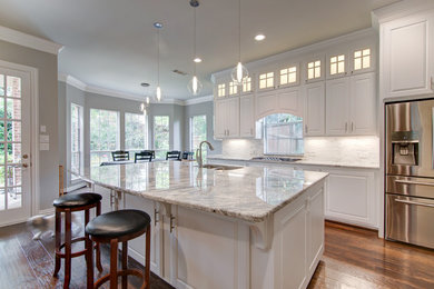 Example of a large transitional galley medium tone wood floor and brown floor open concept kitchen design in Dallas with an undermount sink, raised-panel cabinets, white cabinets, granite countertops, gray backsplash, stone tile backsplash, stainless steel appliances, an island and gray countertops