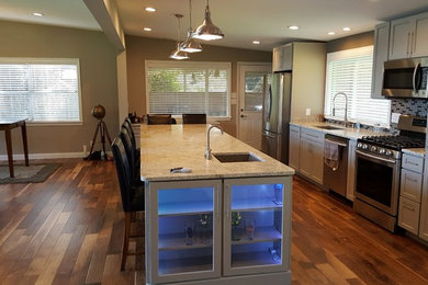 Open concept kitchen - mid-sized transitional galley medium tone wood floor open concept kitchen idea in Indianapolis with an undermount sink, shaker cabinets, gray cabinets, granite countertops, gray backsplash, glass tile backsplash, stainless steel appliances and an island