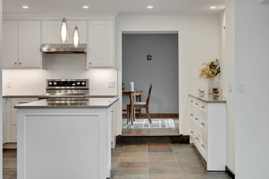 Example of a classic u-shaped slate floor and multicolored floor eat-in kitchen design in Calgary with an undermount sink, shaker cabinets, white cabinets, quartz countertops, white backsplash, subway tile backsplash, stainless steel appliances, an island and beige countertops