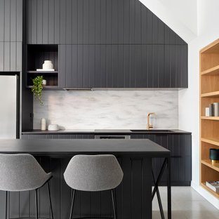 This is an example of a large contemporary l-shaped kitchen in Melbourne with an integrated sink, louvered cabinets, black cabinets, grey splashback, stainless steel appliances, with island, grey floor and black benchtop.