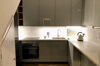 Inspiration for a medium sized modern u-shaped kitchen/diner in London with an integrated sink, flat-panel cabinets, white cabinets, laminate countertops, white splashback, ceramic splashback, black appliances, ceramic flooring, a breakfast bar, brown floors, beige worktops and a drop ceiling.