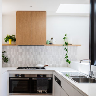 This is an example of a contemporary u-shaped kitchen in Melbourne with a drop-in sink, flat-panel cabinets, white cabinets, white splashback, mosaic tile splashback, stainless steel appliances and white benchtop.