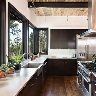 Modelo de cocina en U, contemporánea, grande, con fregadero sobremueble, armarios con paneles lisos, electrodomésticos de acero inoxidable, una isla, puertas de armario negras, encimera de mármol, salpicadero blanco y suelo de madera en tonos medios