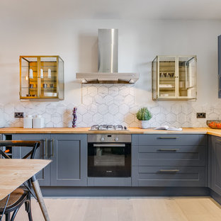 Classic l-shaped kitchen/diner in London with shaker cabinets, blue cabinets, wood worktops, white splashback, light hardwood flooring and beige floors.