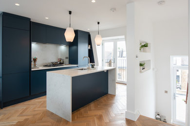 Traditional kitchen in London with flat-panel cabinets, blue cabinets, quartz worktops, white splashback, integrated appliances, medium hardwood flooring, an island and multicoloured worktops.