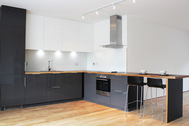 Photo of a large modern l-shaped open plan kitchen in London with an integrated sink, glass-front cabinets, yellow cabinets, engineered stone countertops, white splashback, black appliances, medium hardwood flooring and a breakfast bar.
