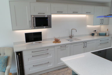 Medium sized modern galley kitchen/diner in Other with a submerged sink, shaker cabinets, white cabinets, quartz worktops, integrated appliances, vinyl flooring, an island, white floors and white worktops.